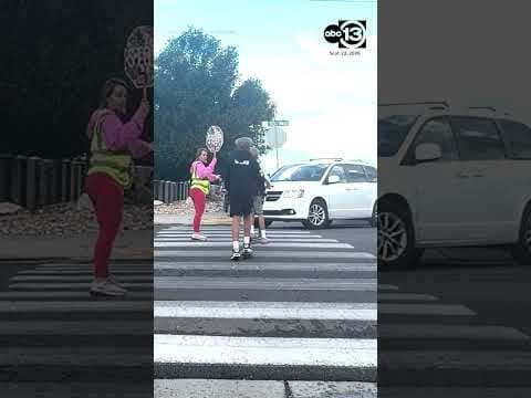 Crossing guard stops minivan from hitting kids on scooters.